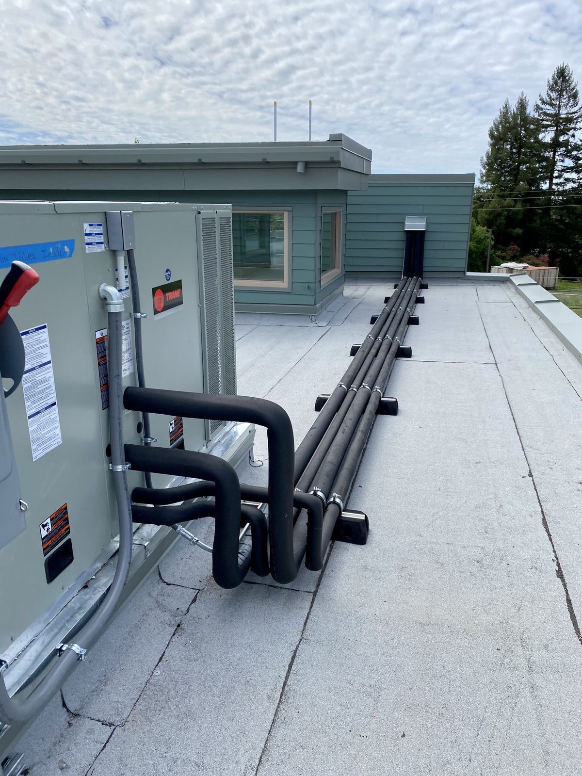 Trane rooftop unit with insulated refrigerant pipework running across a commercial roof.